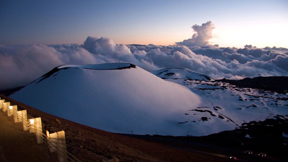 An observatory above a sea of clouds on Maunakea at sunset.